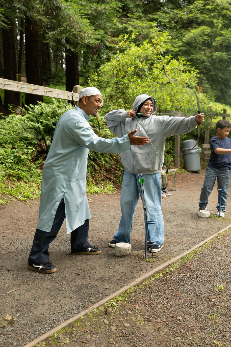 A Futuwwah 5 instructor coaching a young student's archery stance in the forest
